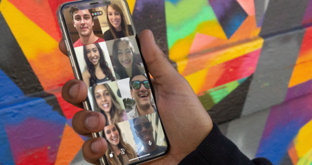 a person holding a phone displaying a video chat with multi people in front of a colorfully painted wall