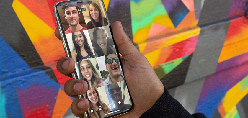 a person holding a phone displaying a video chat with multi people in front of a colorfully painted wall