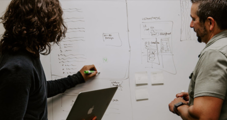 a person writing on a whiteboard while someone else watches