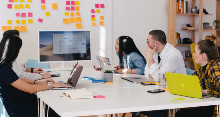 igroup of people sitting at a white table having a work meeting